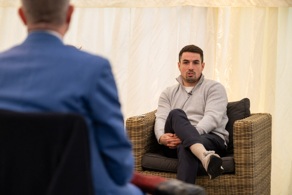 A male Gordon Moody alumni wearing a grey jumper speaks on stage at the official opening event for Gordon Moody House in Redditch on Monday 25th November 2024.