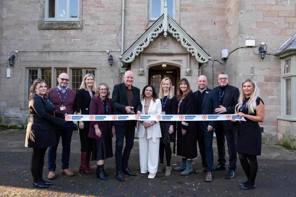 The image shows a group of Gordon Moody colleagues and former professional footballer Steve Bull cutting a white Gordon Moody branded ribbon at the official opening of Gordon Moody House in Redditch on Monday 25th November 2024.