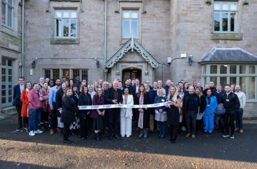 Attendees at the official opening of Gordon Moody House in Redditch on Monday 25th November 2024 pictured behind the branded Gordon Moody ribbon with Steve Bull preparing to cut it.