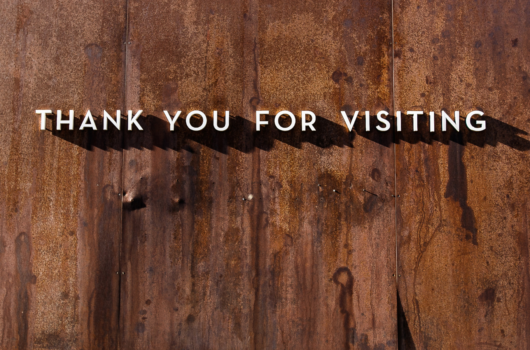 Thank you for visiting sign made of white individual letters lined up on a wooden plank background